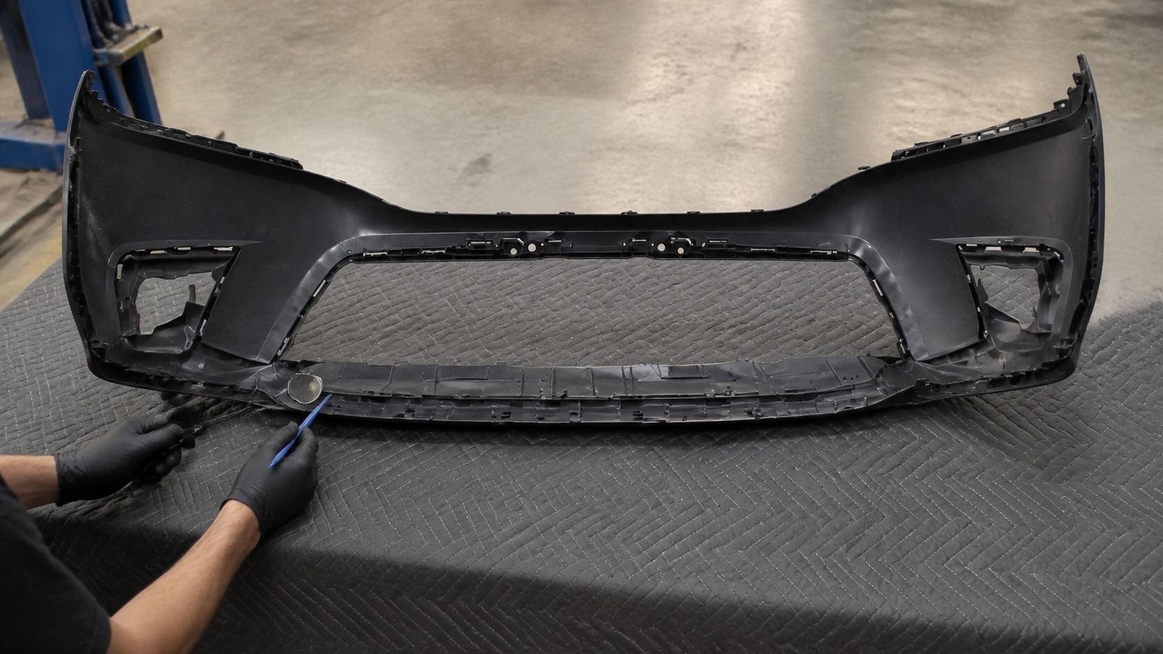 Technician inspecting front bumper mounting tabs and attachment points on a workbench