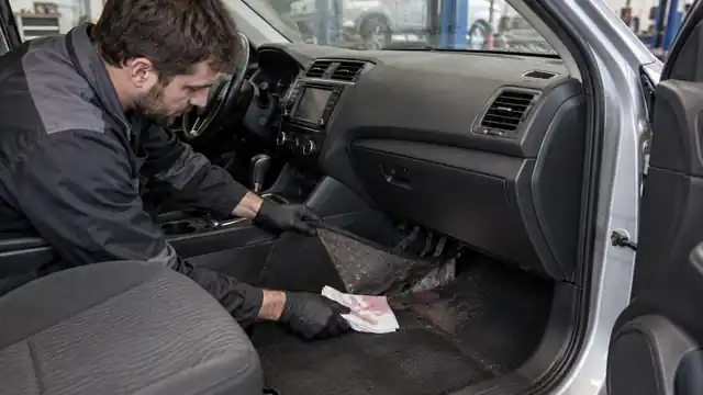 Technician inspecting damp passenger carpet for signs of a leaking heater core